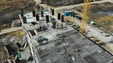 İnşaat alanındaki işçilerin havadan görünüşü ve arka planda vinç.