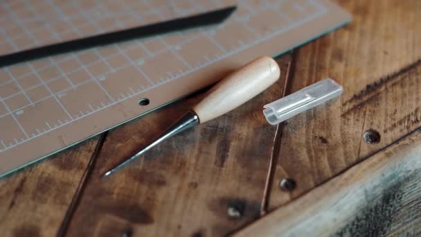 男性の手のクローズアップは、革製品を作るための木製のテーブルの上に横たわるツールを取る — ストック動画