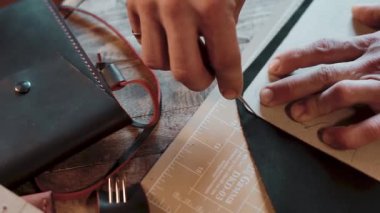 Bir zanaatkar atölyedeki ahşap masanın desenine göre deri kesiyor.