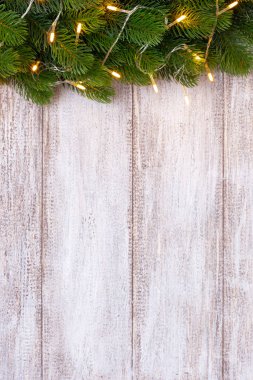 Tahta arka planda sarı bir çelenkle süslenmiş bir Noel ağacının maketi.