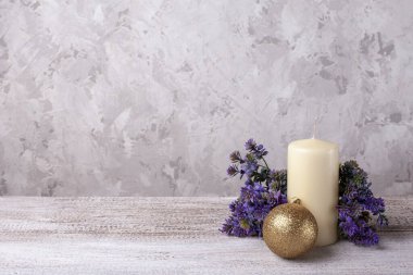 Mor sulu, kalın bej bir mum ve ahşap bir masanın üzerinde altın bir top.