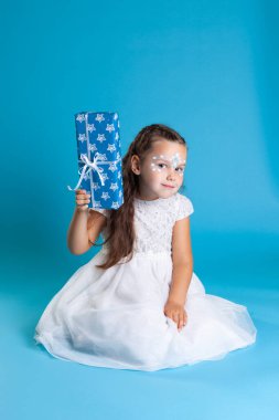 Beyaz elbiseli ve yüzünde kar tanesi makyajı olan uzun boylu bir kız gözünün önündeki kutuyu sallıyor ve tahmin et bakalım orada ne var?