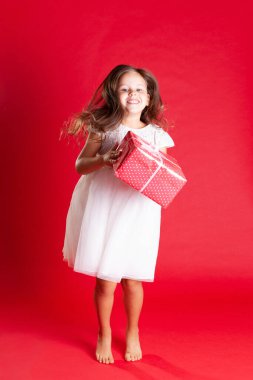 Beyaz gelinlikli uzun boylu kız mutlulukla zıpla ve Noel hediyesini ya da doğum gününü kırmızı arka planda tut.