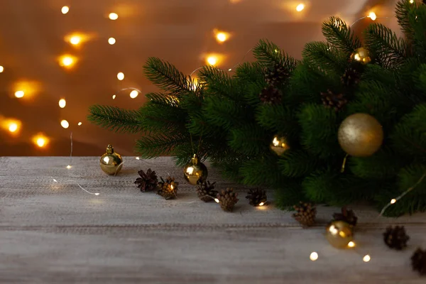 Árbol de Navidad decorado con bolas de oro sobre una mesa de madera en pintura blanca en el resplandor de las tibias guirnaldas — Foto de Stock