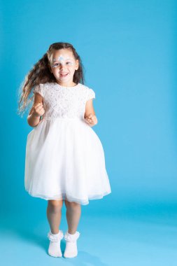 Beyaz melek elbisesi içinde uzun boylu, gülümseyen bir kız mavi bir arka planda zevkten zıplar ya da dans eder.