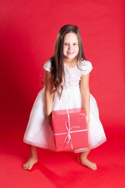 Beyaz elbiseli güzel esmer çocuk Noel 'de ya da kırmızı arka planda doğum gününde hediye kutusunu yerden aldı.