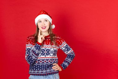 Noel süveteri ve Noel Baba şapkası giymiş, kırmızı arka planda bir fotokopi odası olan düşünceli genç bir kadını kapatın.