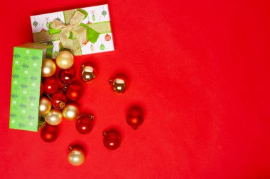 Kırmızı arka planda Noel ağacı için dağınık kırmızı ve altın toplarla birlikte açık yeşil hediye kutusuyla süslenmiş.