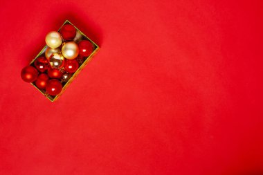 Doymuş bir arka planda Noel ağacı için kırmızı ve altın topları olan yeşil bir hediye kutusundan kartpostal.