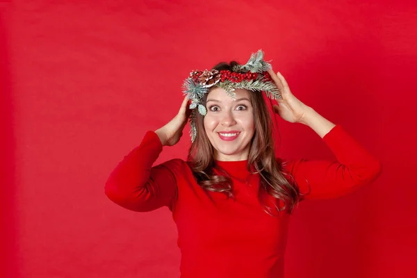 Giovane donna sorpresa con i capelli ricci, che si tiene per mano o regola una corona di Natale sulla testa, con spazio per il testo — Foto Stock