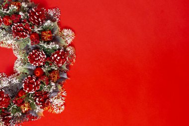 Kırmızı arka planda izole edilmiş koni ve böğürtlenli, ladin dallarından yapılmış yarım bir Noel çelengi.