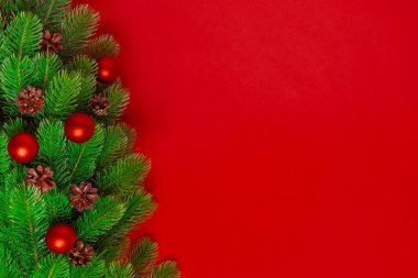 Noel ağacının dallarından alınmış bir kartpostal. Çam kozalakları ve doymuş arka planda kırmızı toplar var. Boşluğu kopyala.