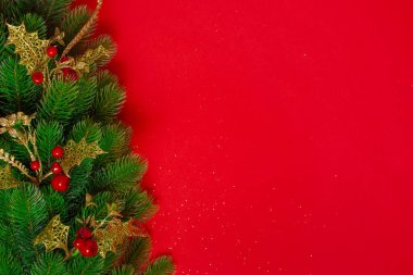 Kırmızı arka planda izole edilmiş, altın dekoru ve kırmızı böğürtlenli bir Noel ağacı çelengi.