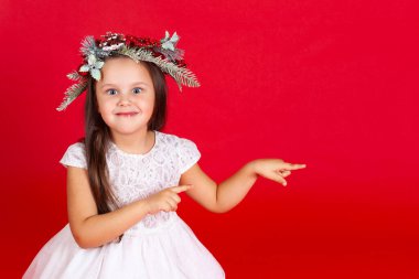 Kırmızı arka planda işaret parmaklarıyla işaret eden, tatil elbisesi giymiş şaşırmış bir kızın portresi.