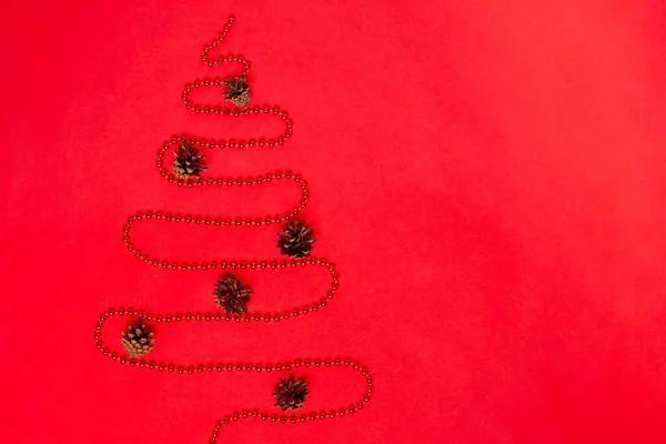 postcard from a garland of beads laid out in the form of a Christmas tree with decorations from cones, isolated on a red background, mock up