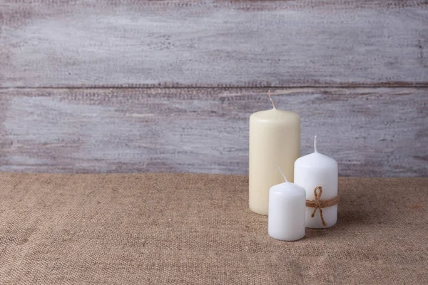 mock up of two white candles in jute rope and a vanilla candle on a wooden background and burlap