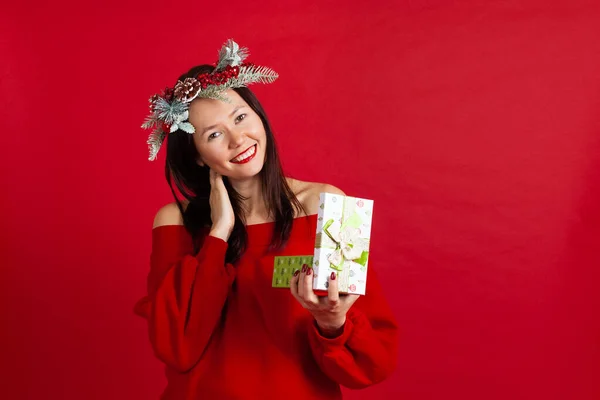 Close-up portret van een lachende Aziatische jonge vrouw in een kerstkrans met rode lippenstift genieten van een nieuw jaar cadeau — Stockfoto