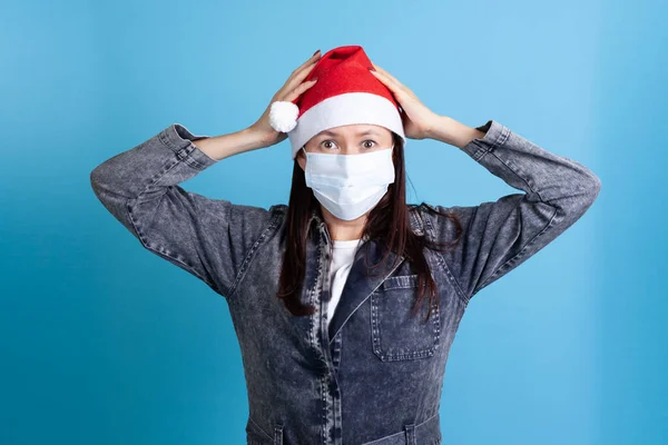 Asustada mujer asiática con sombrero de Santa y máscara de protección médica contra el virus, sosteniendo la cabeza con las manos —  Fotos de Stock