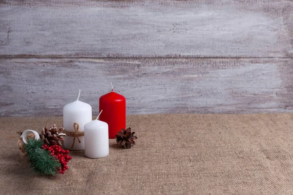 mock up of two white candles in jute rope and a red candle, cones, a sprig of a Christmas tree decorated with berries