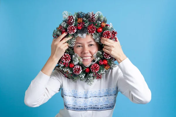 Portret van een Aziatische jonge vrouw kijkend door een kerstkrans van boomtakken, kegels en ornamenten — Stockfoto