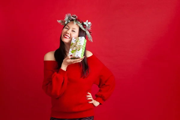 Mock up glimlachen mooi aziatisch jong vrouw in een kerstkrans genieten van een nieuw jaar cadeau, op een rode achtergrond — Stockfoto