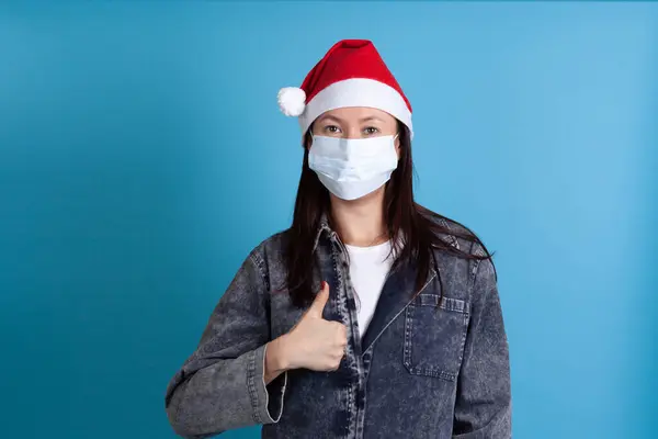 Primer plano de una joven asiática con un sombrero de Santa y una máscara de protección médica contra el virus, protección confiable —  Fotos de Stock