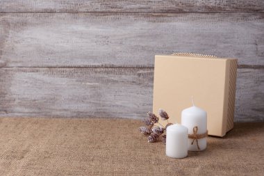 Jüt halat ve bej hediye kutusundaki iki beyaz mumla ahşap bir arka planda koni yap.
