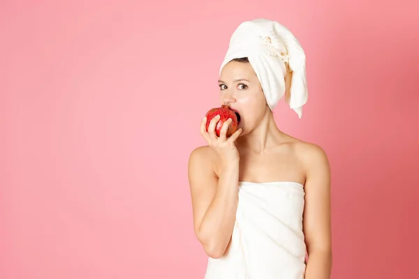 Mock up, retrato de uma jovem mulher com uma toalha na cabeça e em seu corpo mordendo uma romã vermelha isolada em um fundo rosa — Fotografia de Stock