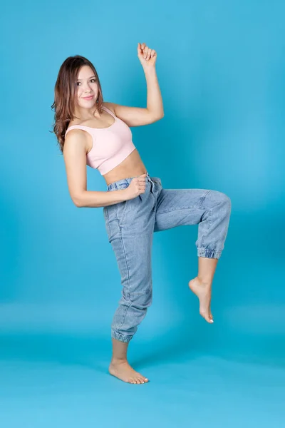 Una mujer atlética de cuerpo entero en jeans y un top rosa baila aislado sobre un fondo azul — Foto de Stock