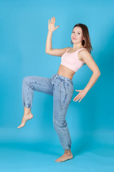 Una joven de cuerpo entero en jeans baila como Pinocho aislado sobre un fondo azul — Foto de Stock