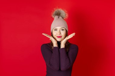 Kış şapkası ve elleri örülmüş, kırmızı bir arka planda soyutlanmış, gülümseyen genç bir kadını yakından çek.