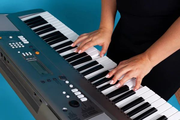 Close-up of female hands and fingers of a woman playing an electronic synthesizer, isolated on a blue background — Stock Photo, Image