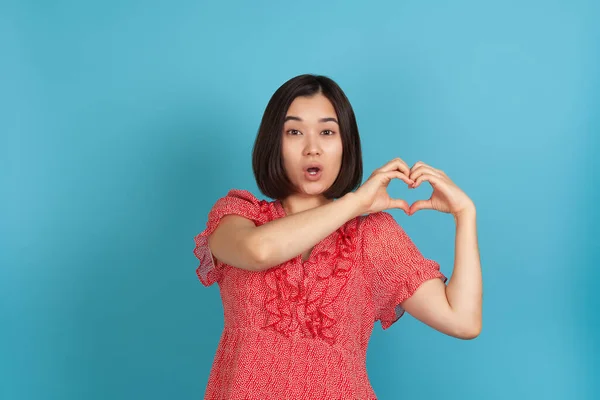 Close-up verrast open-mouthed jong aziatisch vrouw maakt hart symbool van vingers geïsoleerd op blauwe achtergrond — Stockfoto
