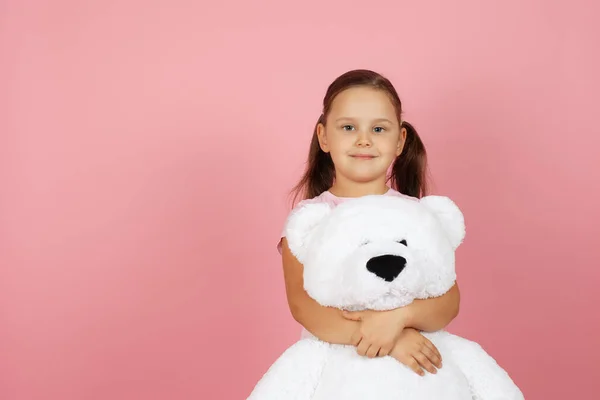 Mock up schattig, glimlachend meisje met paardenstaarten en in roze jurk knuffels witte teddybeer geïsoleerd op roze achtergrond — Stockfoto