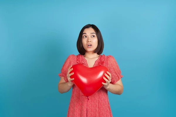 Primer plano sorprendido emocionado mujer asiática sosteniendo rojo corazón en forma de globo en San Valentín día aislado sobre fondo azul — Foto de Stock