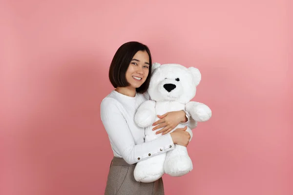 Mock up lachen tevreden jong aziatisch vrouw knuffels wit teddy beer geïsoleerd op roze achtergrond — Stockfoto