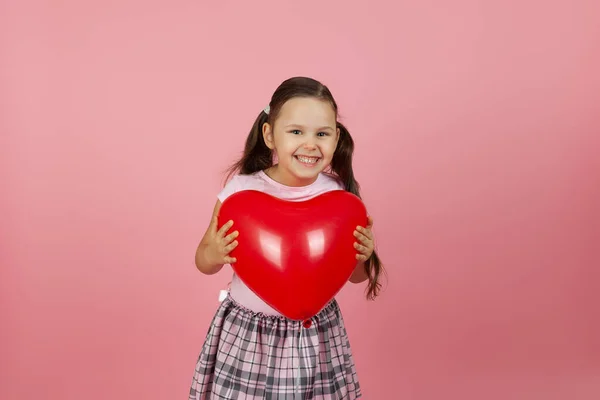 Maqueta de admirar, encantado, chica sorprendida en vestido rosa sosteniendo globo en forma de corazón rojo aislado sobre fondo rosa — Foto de Stock