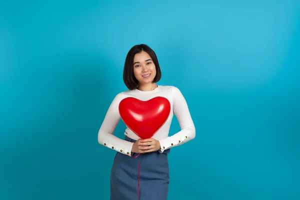 Mock up gelukkig jong glimlachen aziatische vrouw houden rood hartvormige ballon geïsoleerd op blauwe achtergrond — Stockfoto