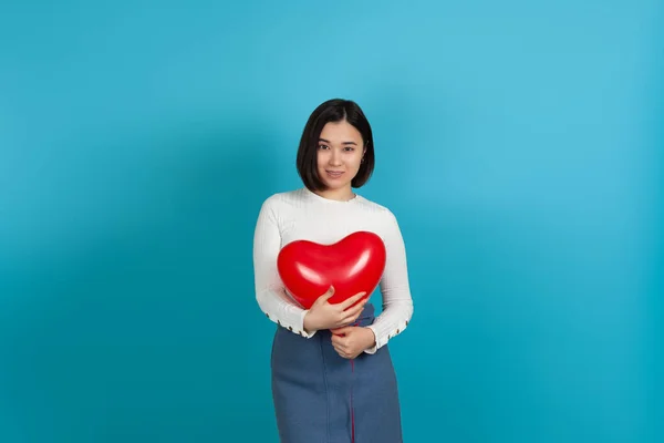 Mooi jong glimlachen aziatisch vrouw knuffels rood hartvormige ballon geïsoleerd op blauw achtergrond — Stockfoto