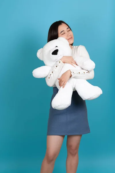 Charmant jong aziatisch vrouw met haar ogen dicht strak knuffels een groot wit teddy beer valentijnsdag geschenk geïsoleerd op een blauwe achtergrond — Stockfoto