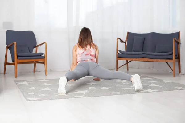 Visão traseira de uma mulher em leggings cinza em Surya Namaskara em um interior de casa — Fotografia de Stock