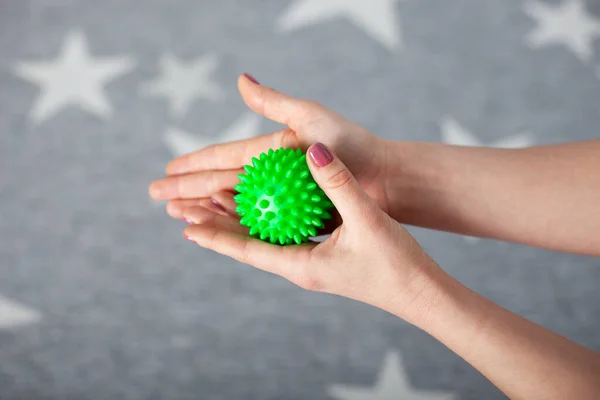 Primer plano dos palmas femeninas sostienen una bola de masaje de púas verdes contra una alfombra gris con estrellas blancas —  Fotos de Stock