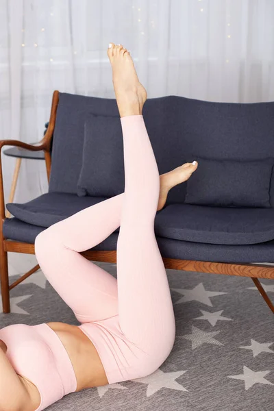 Крупним планом ноги жінки в рожевих спортивних легінсах підняті на сірому м'якому дивані інтер'єр будинку — стокове фото
