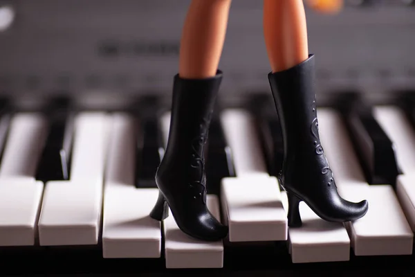 Close-up slim plastic legs in black toy rubber boots with high heels step on piano keys — Stock Photo, Image