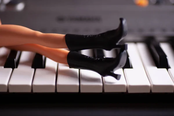 Close-up slim plastic legs in black toy rubber boots with high heels lie on piano keys — Stock Photo, Image
