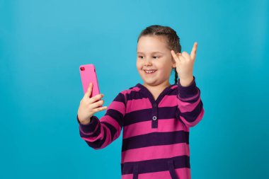 Saçları örgülü, telefonla konuşan, kol mesafesinde telefonu tutan ve boynuzlarını parmaklarıyla gösteren bir kızın yakın plan portresi.