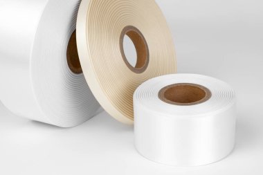 Etiketler ya da markalar için farklı boyutlarda beyaz, bej saten şeritlerden oluşan üç bobin bobininin makro bileşimi, beyaz, gri bir arkaplanda izole edilmiş.