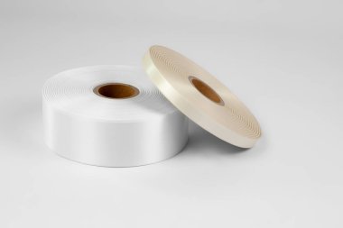 Etiketler için iki makara saten kurdele ya da beyaz ve bej dikmek, beyaz ve gri bir arkaplanda izole edilmiş.