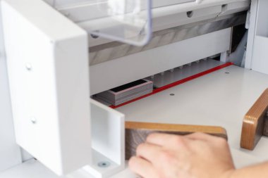 Uzman operatör otomatik kağıt kesme makinesi, profesyonel kesici, matbaa veya atölye ekipmanı üzerinde çalışır.