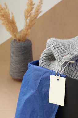 Siyah bir kutuda gri örülmüş bir eşarp ve bej kağıda sarılı bir vazo içinde kurutulmuş pampa otu üzerinde makro beyaz kağıt logo etiketi.